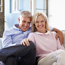 Older couple sitting on couch and smiling after bruxism treatment