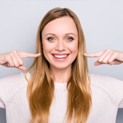 Woman pointing at her smile after dental crown restoration
