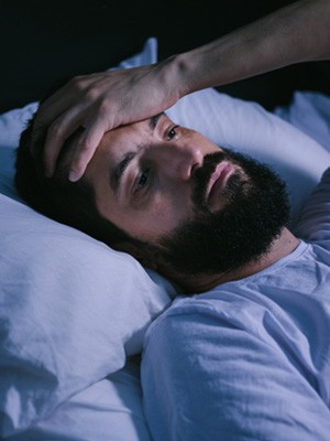 Restless man in bed holding his hand to his forehead