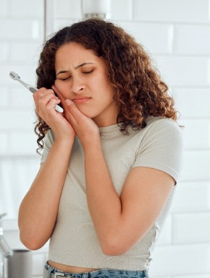 Woman with toothbrush touching sore jaw with eyes closed