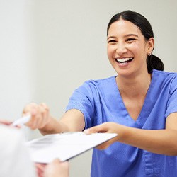 Dental assistant smiling while handing patient form