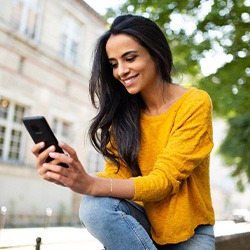 Woman smiling while looking at phone outside