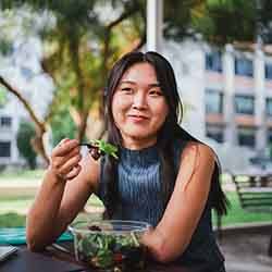 Woman smiling while eating salad at park outside